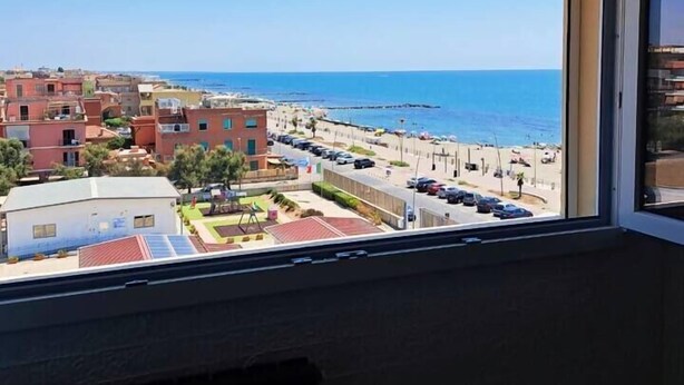 Vista desde una ventana sobre una playa con edificios y coches aparcados.