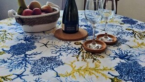Una mesa de comedor con mantel floral, una botella de vino, un cuenco de fruta y dos copas de vino.