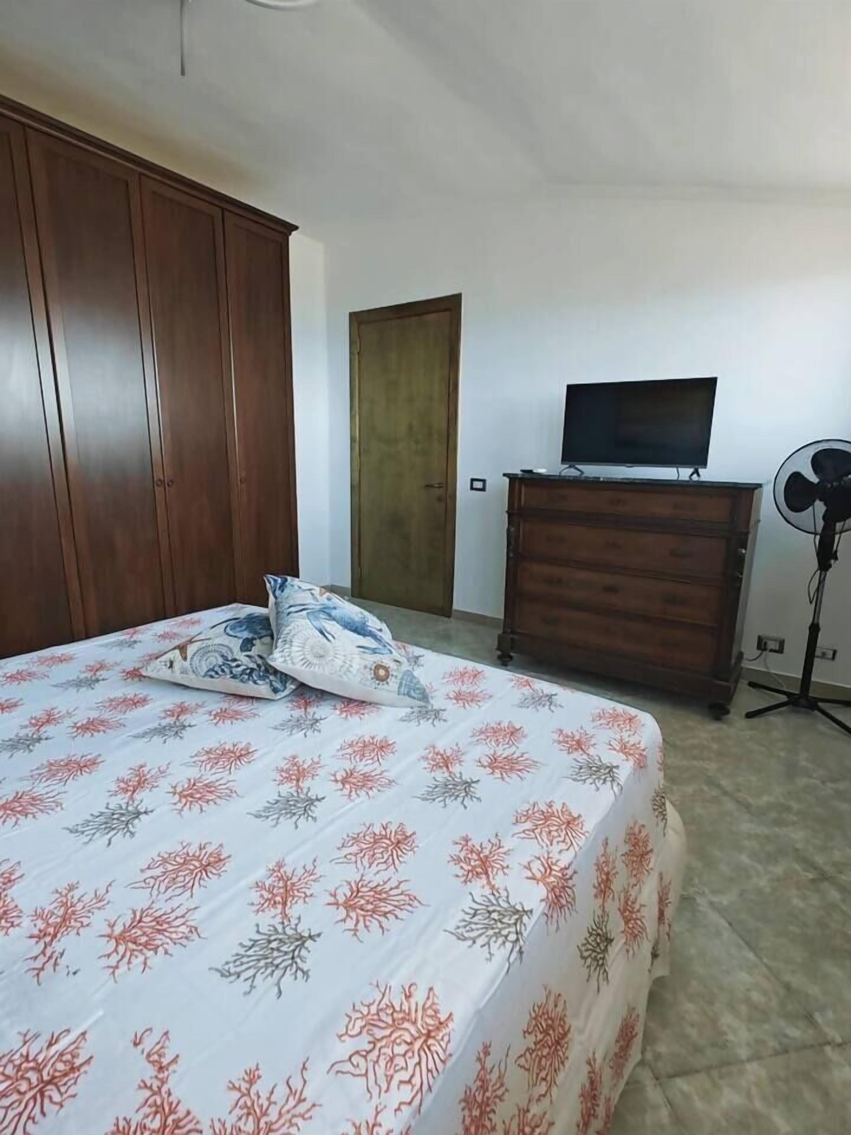A bedroom with a bed, a dresser, a television, and a fan.
