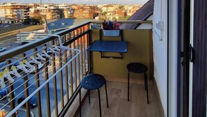 Un balcón con una mesa y dos sillas, con vistas a un paisaje urbano con edificios y una carretera.