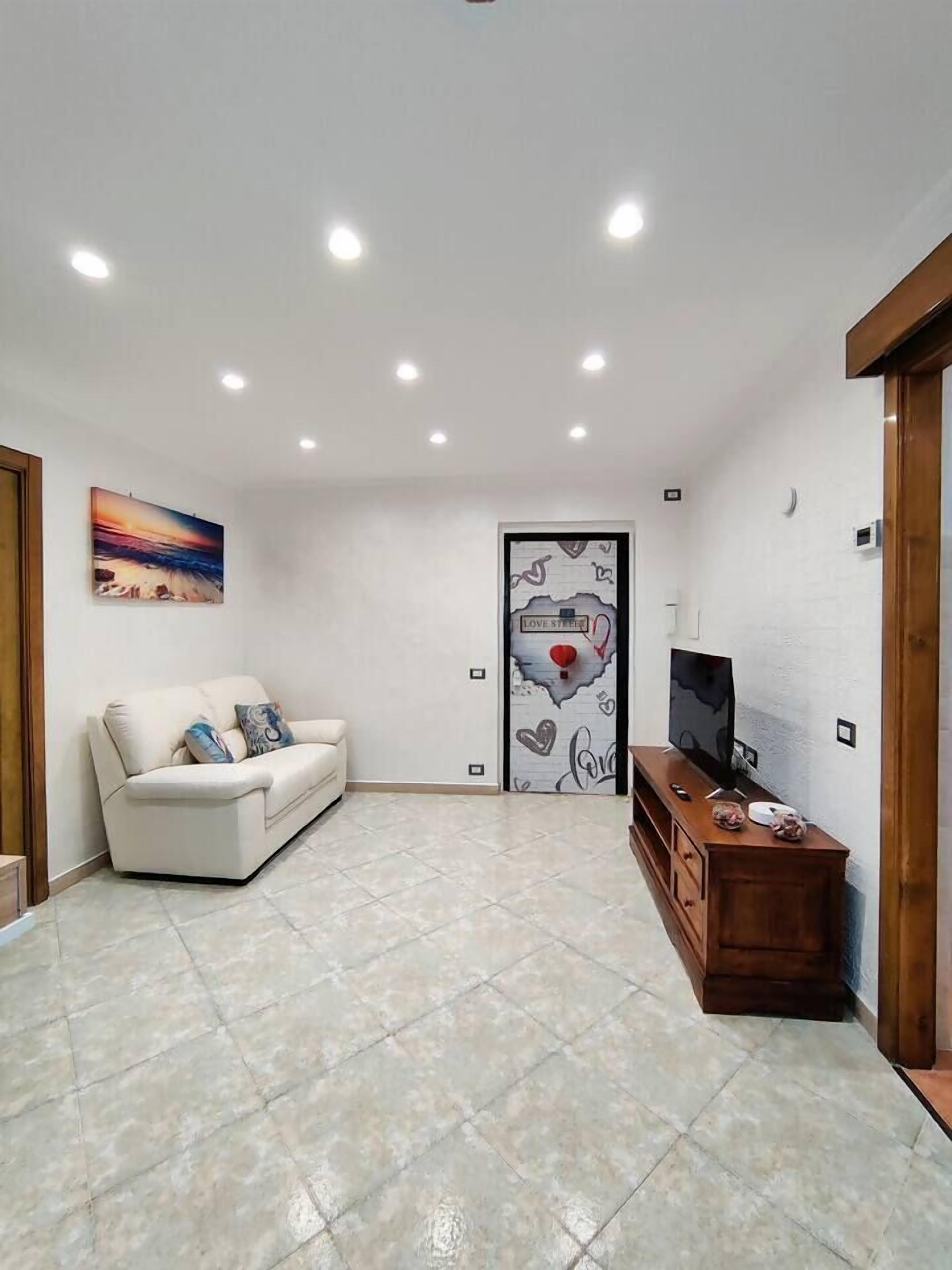 A spacious living room with a white sofa, a wooden cabinet, and a TV.