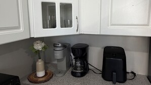 A kitchen with white cabinets, a coffee maker, an air fryer, and a vase with flowers on the counter.