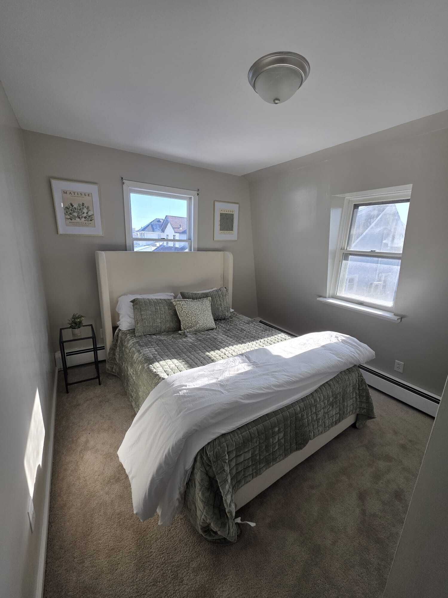 Une chambre à coucher avec un lit, une fenêtre et deux tableaux encadrés accrochés au mur.