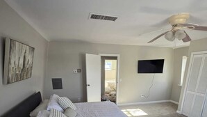 A bedroom with a bed, a ceiling fan, a TV, and a door leading to another room.