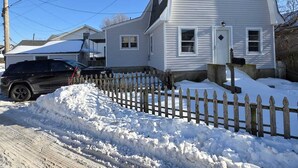A two-story house with a white exterior, a wooden picket fence, and a black SUV parked in front.