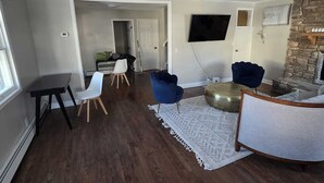 A spacious living room with hardwood flooring, a stone fireplace, and a television mounted on the wall.