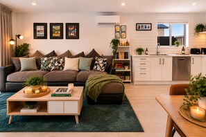 A modern living room with a sofa, coffee table, and a kitchen area with a dishwasher and sink. - Shotover Serenity (Queenstown)