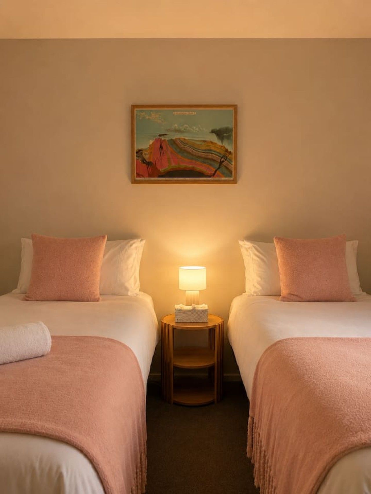 A hotel room with two beds, a nightstand with a lamp, and a painting on the wall.