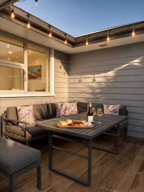An outdoor seating area with a table set for two, a sofa, and a window with a painting. - Shotover Sanctuary - 2 Bedroom home! (Queenstown)