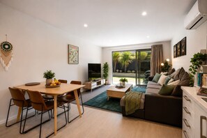 Uma sala de estar moderna com área de jantar, sofá, mesa de centro e televisão.