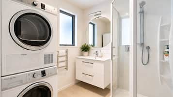 A modern bathroom with a washing machine, a shower, and a vanity with a mirror.
