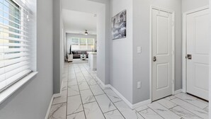 A hallway with white marble flooring, a white door on the right, and a painting on the wall. - Savvy 4Bed Stay Near Orlando Attractions (Kissimmee)