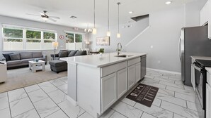 A modern kitchen with a central island, white cabinetry, and a stainless steel refrigerator. - Savvy 4Bed Stay Near Orlando Attractions (Kissimmee)