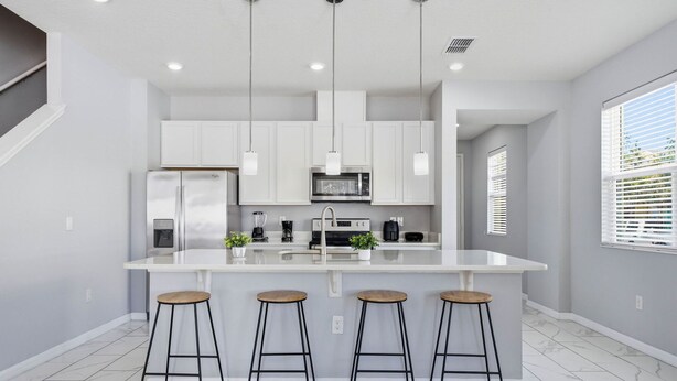 A modern kitchen with white cabinets, a central island with stools, and pendant lighting. - Savvy 4Bed Stay Near Orlando Attractions (Kissimmee)
