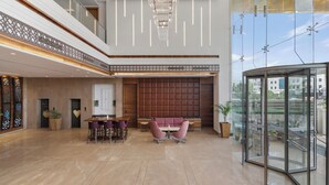 Eine geräumige Lobby mit hoher Decke, einer zentralen Sitzecke und einem Glastreppenaufzug.