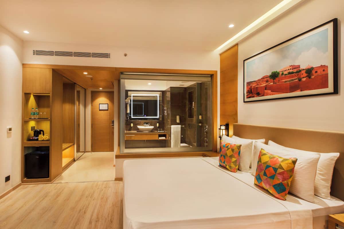 Ein Hotelzimmer mit einem großen Bett, einem Badezimmer mit Spiegel und einem Gemälde an der Wand.