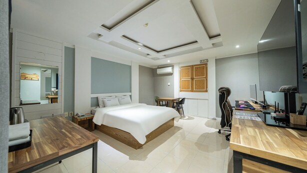 A modern hotel room with a large bed, a desk, a chair, a small table, an air conditioning unit, and a television. - Cat's Hotel (Bucheon)