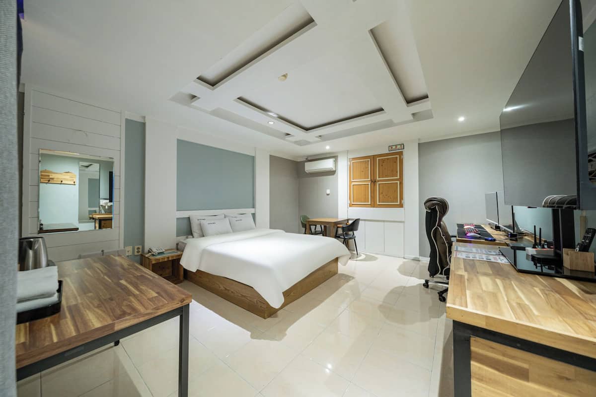 Ein modernes Hotelzimmer mit einem großen Bett, einem Schreibtisch, einem Stuhl, einem kleinen Tisch, einer Klimaanlage und einem Fernseher.