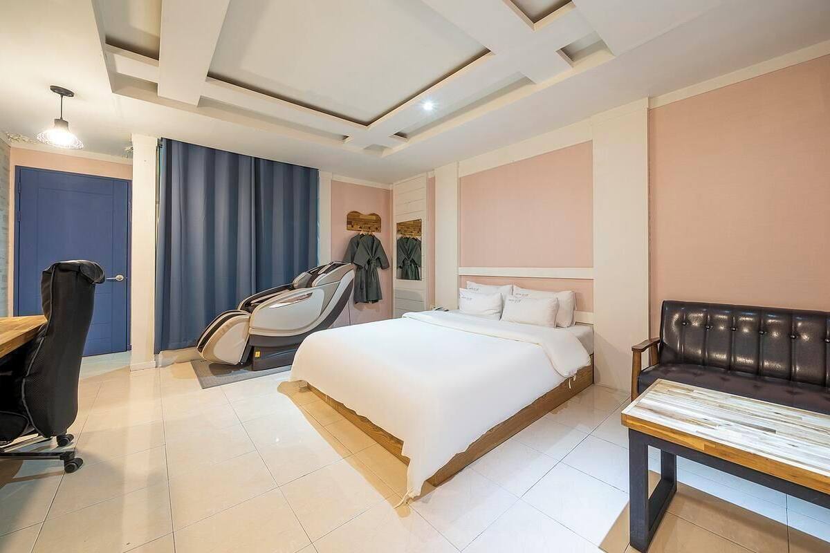 Ein Hotelzimmer mit Bett, Schreibtisch, Stuhl, Massagesessel, Bank und Deckenleuchten.