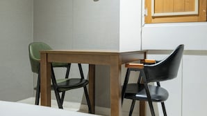 A small dining area with a wooden table and two chairs, one green and one black. - Cat's Hotel (Bucheon)
