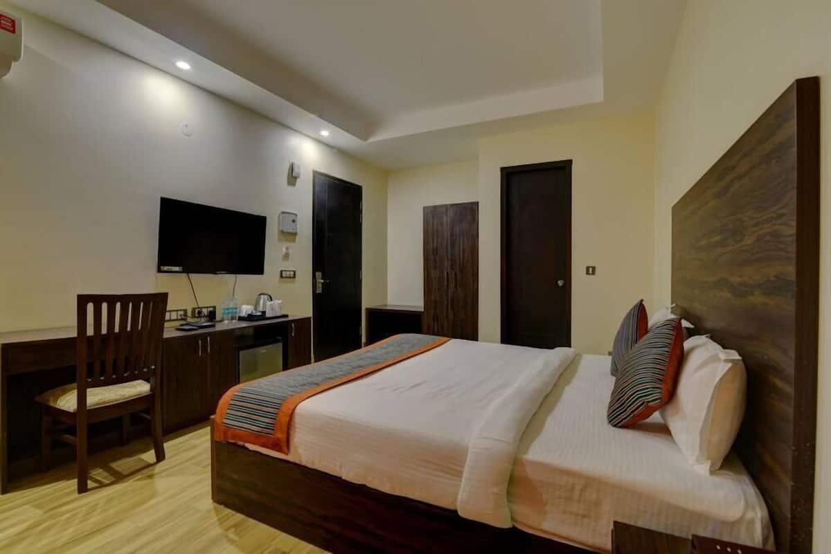 Una camera d'albergo con un letto, una scrivania, una sedia, una televisione e una porta.