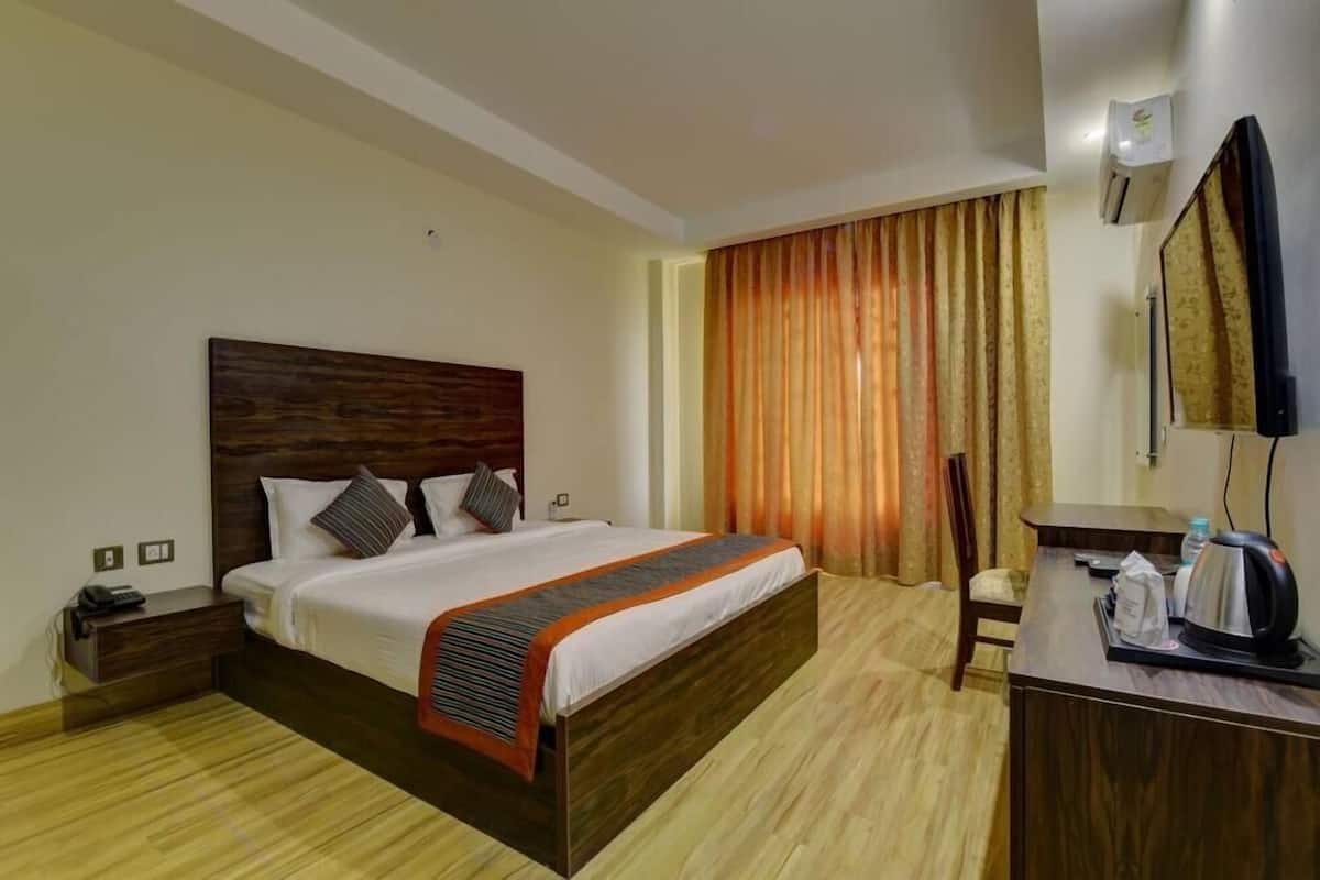 Una camera d'albergo con un letto in legno, un comodino, una scrivania con un bollitore e un'ampia finestra con tende.