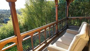 A wooden deck with a cushioned seating area and a view of a forested landscape.