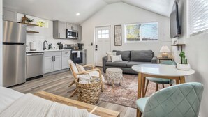 Eine moderne Küche mit Edelstahlgeräten, ein Essbereich mit rundem Tisch und Stühlen, ein graues Sofa und ein Deckenventilator.