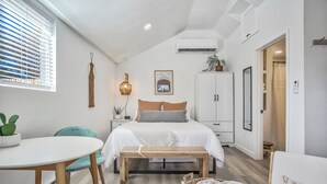 Ein Schlafzimmer mit Bett, Nachttisch, Lampe und einem Fenster mit Jalousien.