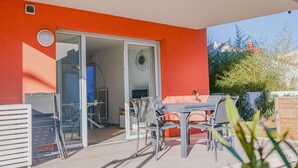 An outdoor patio with a table and chairs, a sliding glass door leading to an interior space, and a view of greenery and a building in the background. - 4-STAR APARTMENT – 2 BEDROOMS – COGOLIN – SWIMMING POOL – CLOSE TO THE TOWN CENTRE (COGOLIN)