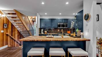 Une cuisine moderne avec des meubles de couleur bleu foncé, un îlot central en bois doté de tabourets et un escalier avec des rampes en bois.