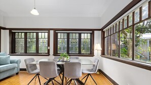 A dining area with a table and chairs, large windows, and a blue sofa. - Relaxing Stay Near Fairlight's Scenic Spots (Sydney)