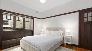 A bedroom with a large bed, two bedside tables with lamps, a window with blinds, and a door. - Relaxing Stay Near Fairlight's Scenic Spots (Sydney)