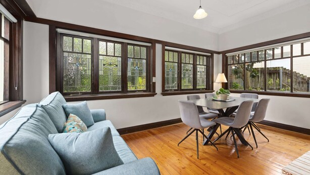 A room with a blue sofa, a dining table with chairs, and large windows with a view of greenery. - Relaxing Stay Near Fairlight's Scenic Spots (Sydney)
