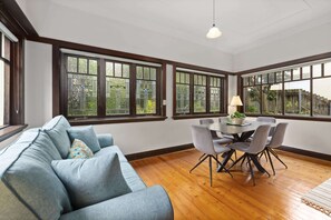 Una habitación con un sofá azul, una mesa de comedor con sillas y ventanas amplias con vistas a zonas verdes.
