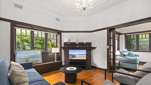 A spacious living room with a fireplace, large windows, a blue sofa, and a grey armchair. - Relaxing Stay Near Fairlight's Scenic Spots (Sydney)