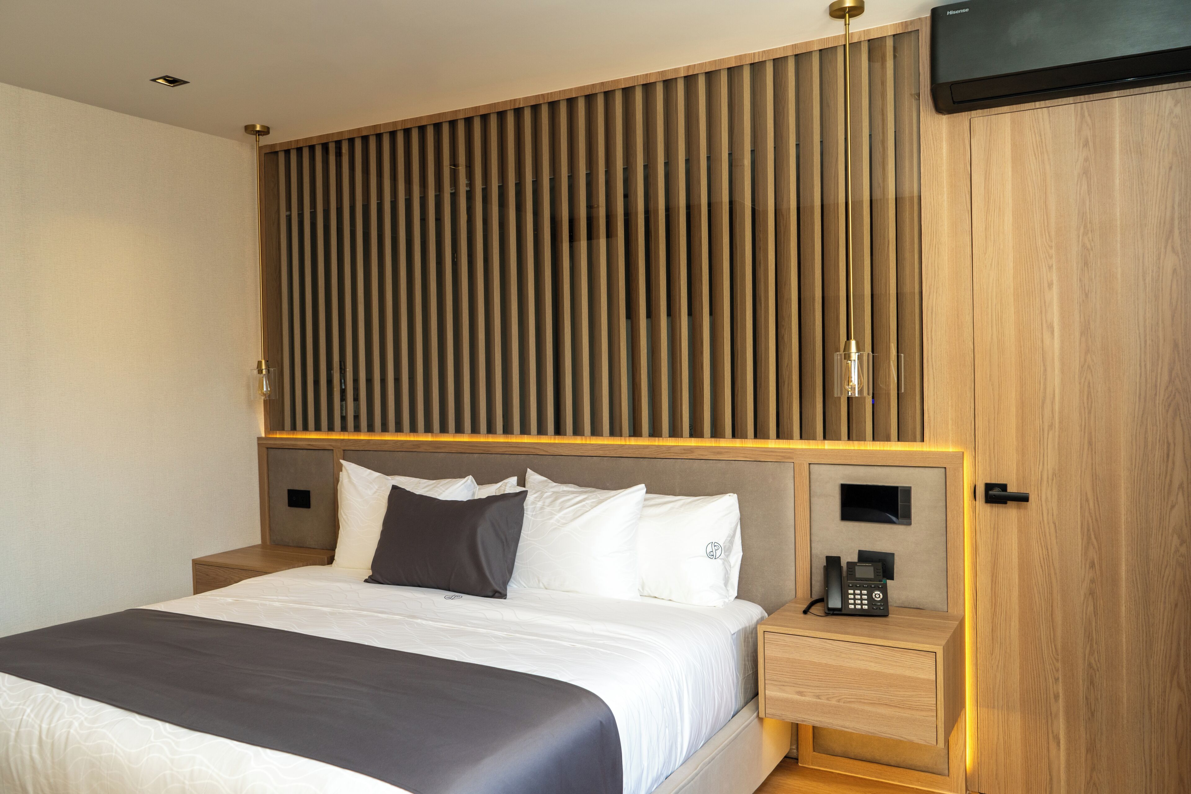 Una habitación de hotel moderna con cama, mesitas de noche, televisor montado y pared de paneles de madera.