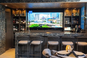 A bar area with a flat-screen TV, bar stools, and a variety of liquor bottles.