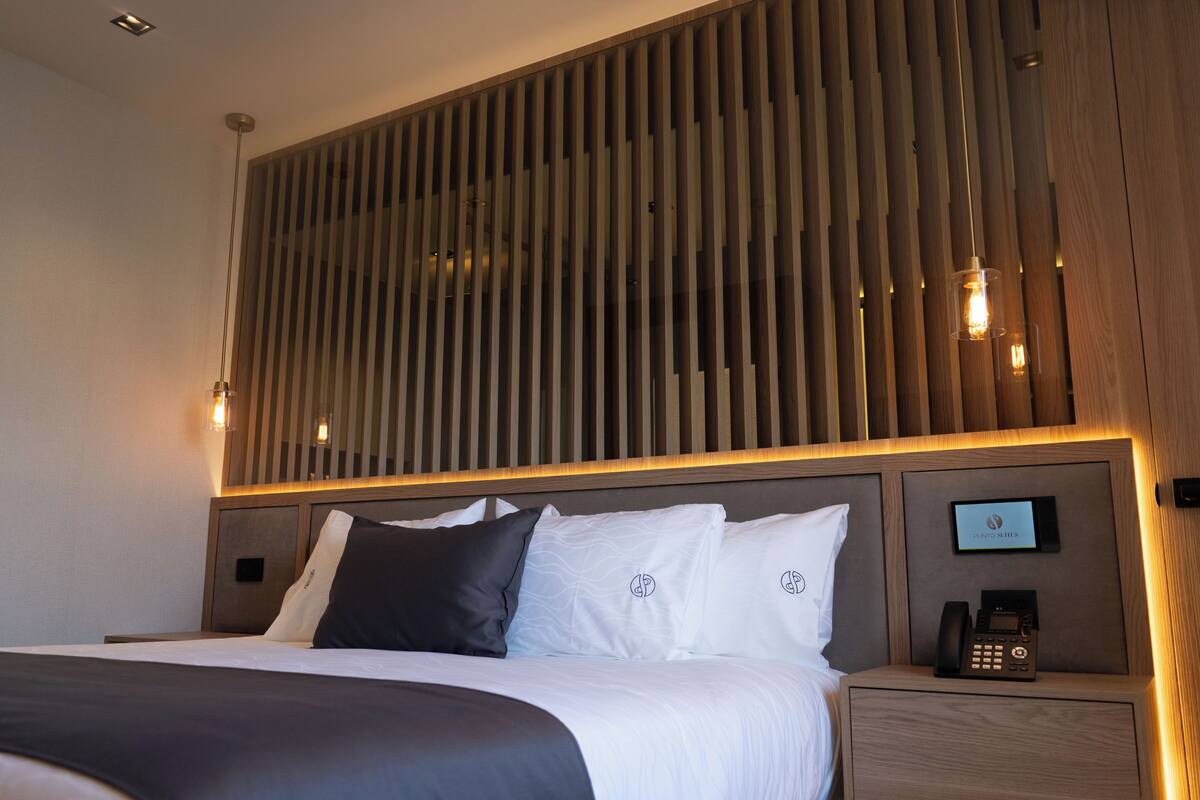 Habitación de hotel con cama, mesita de noche y teléfono, y paneles decorativos en la pared.