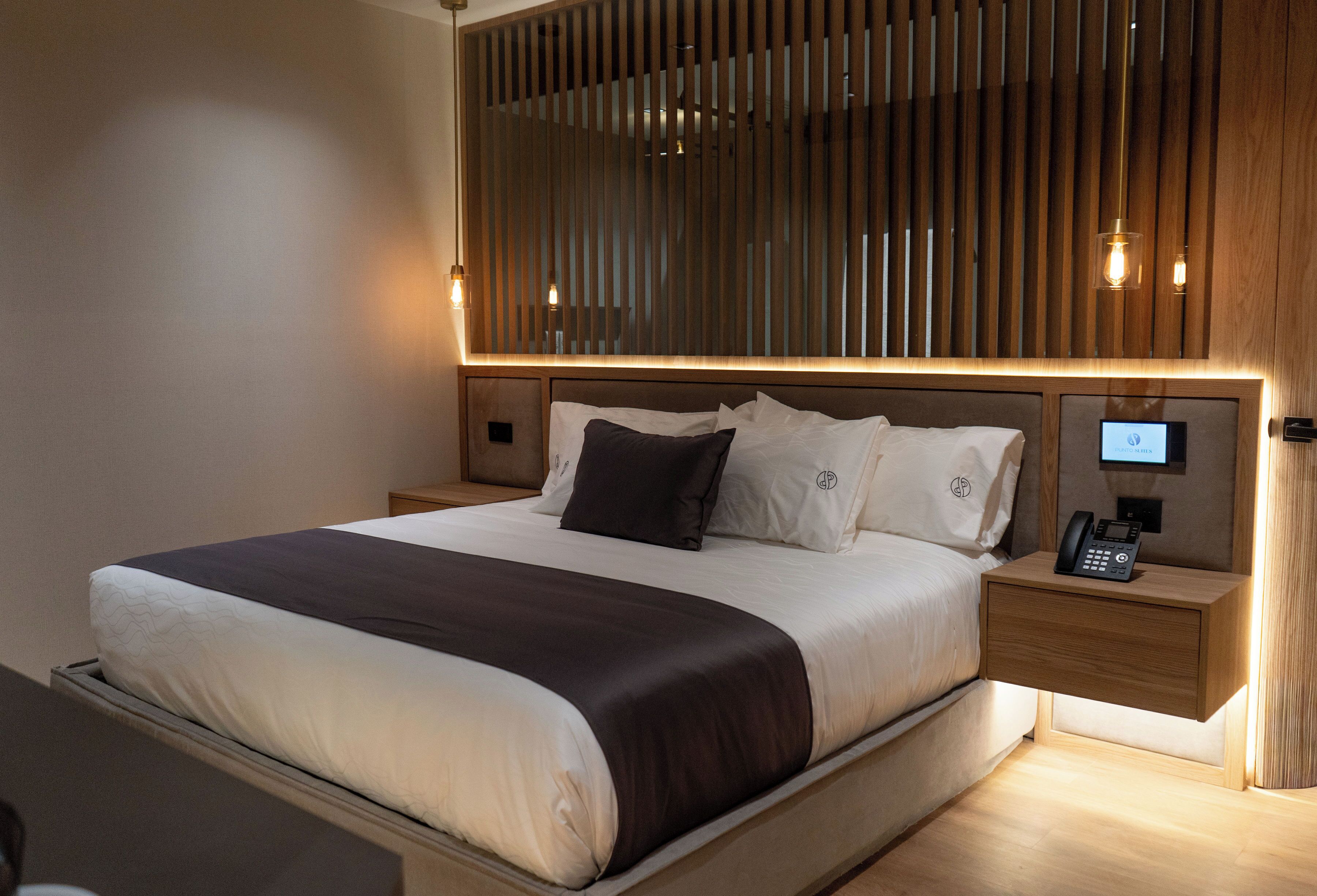 A modern hotel room with a large bed, wooden headboard, bedside tables with lamps, and a built-in phone.