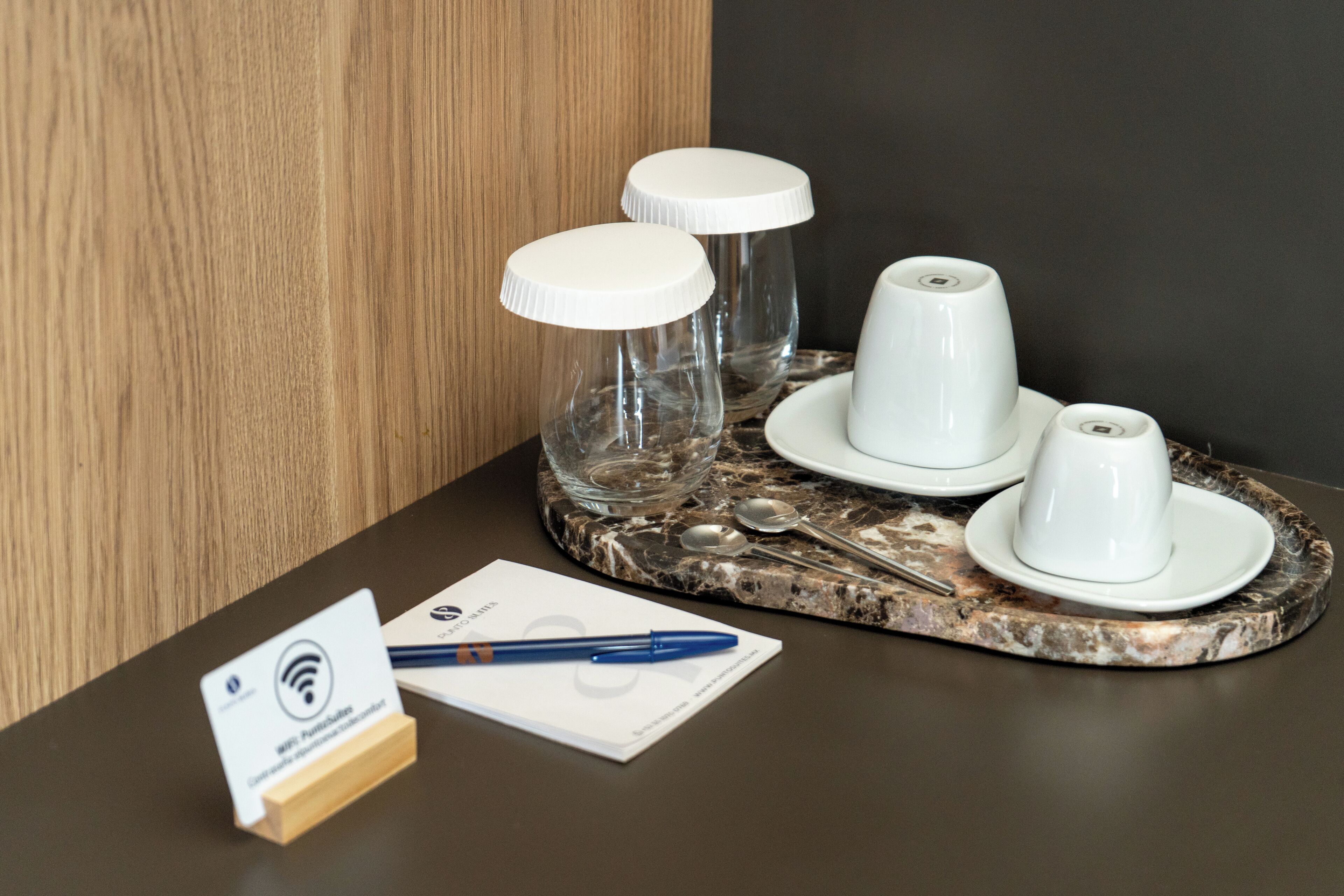 Una bandeja de mármol con tazas y platillos blancos, una cuchara y un bolígrafo sobre una mesa.