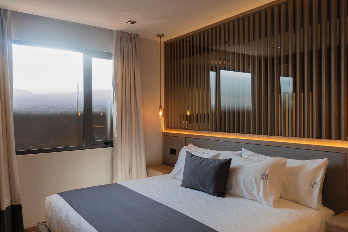Ein Hotelzimmer mit einem großen Bett, Blick auf die Stadt durch das Fenster und einem modernen Design mit vertikalen Holzleisten an der Wand.