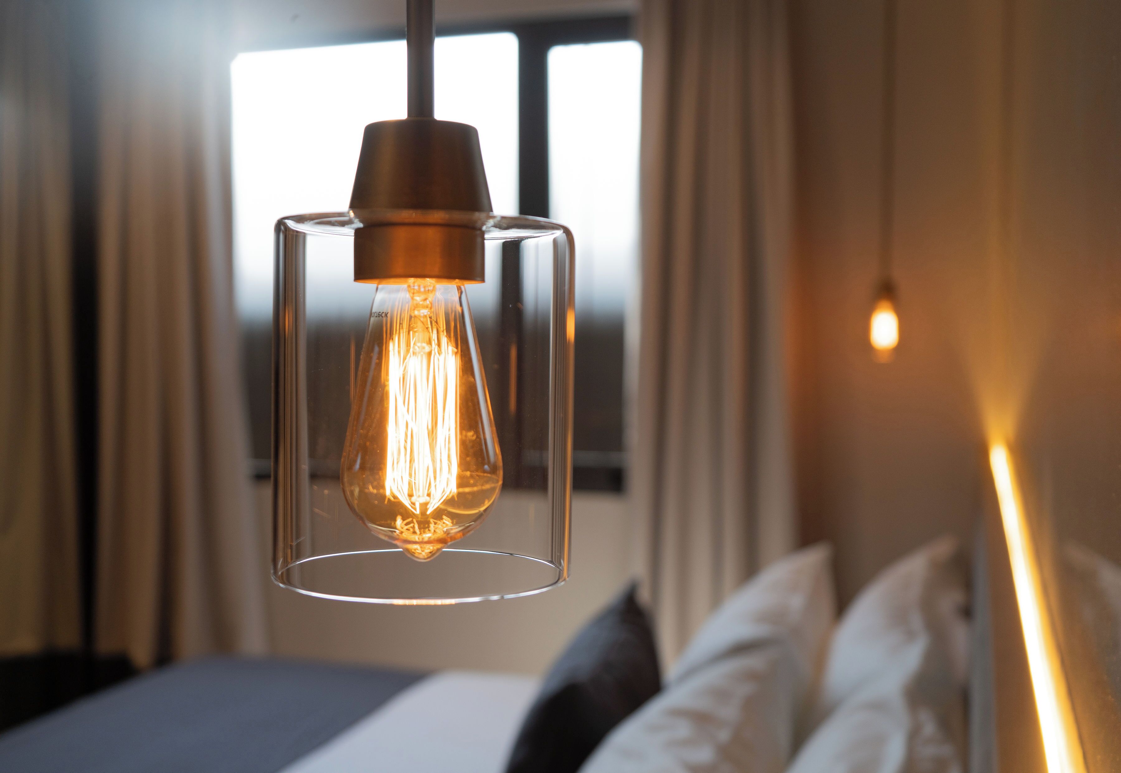Un luminaire suspendu dans une pièce où se trouvent un lit et des rideaux.