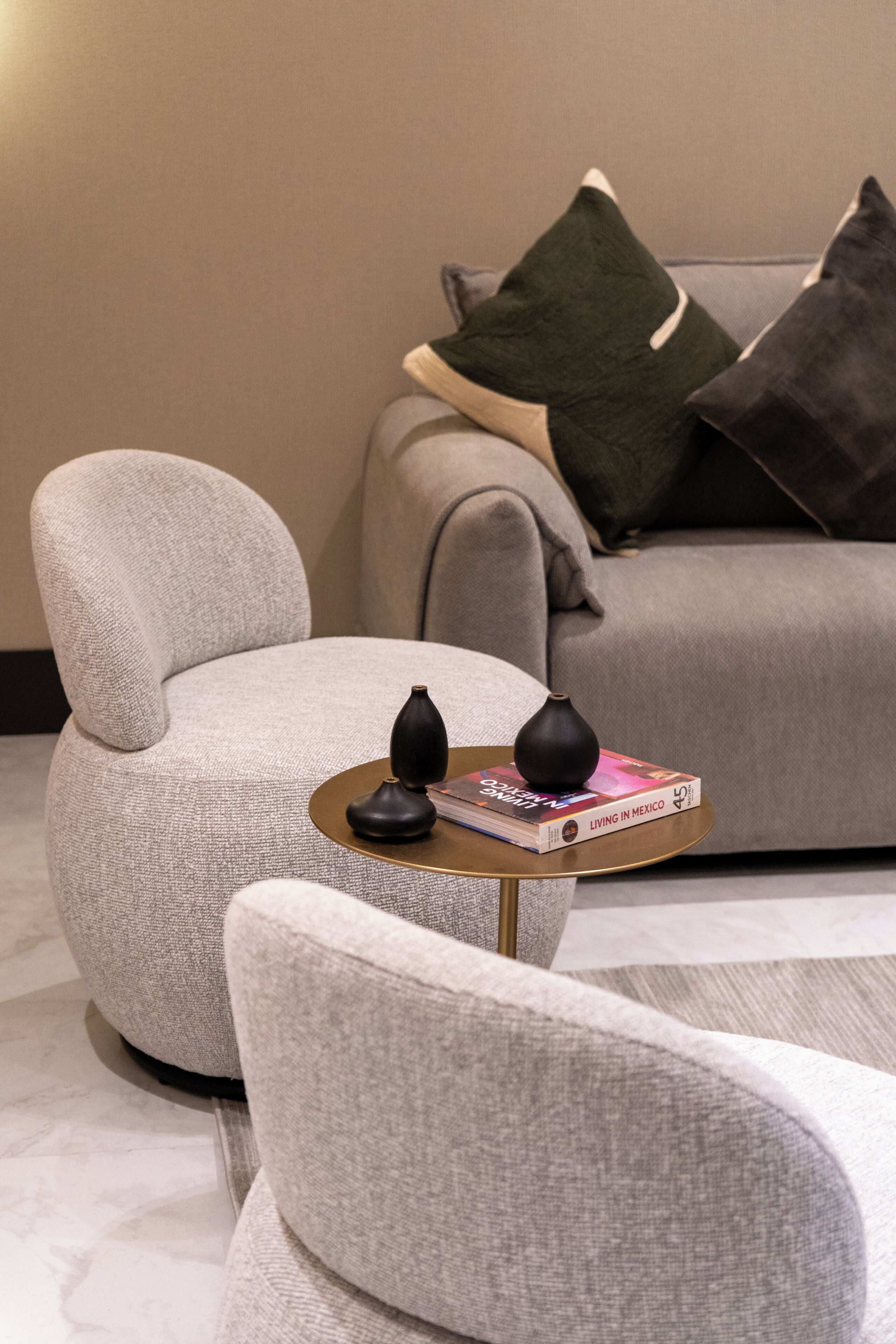 A modern living room with a grey sofa, a matching armchair, and a small round table with a book and a vase.