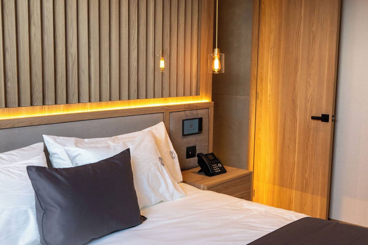 Habitación de hotel con cama, teléfono junto a la cama, televisor montado en la pared y paneles de madera.