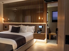 Quarto de hotel moderno com uma cama grande, mesa de cabeceira com telefone e televisão no canto.