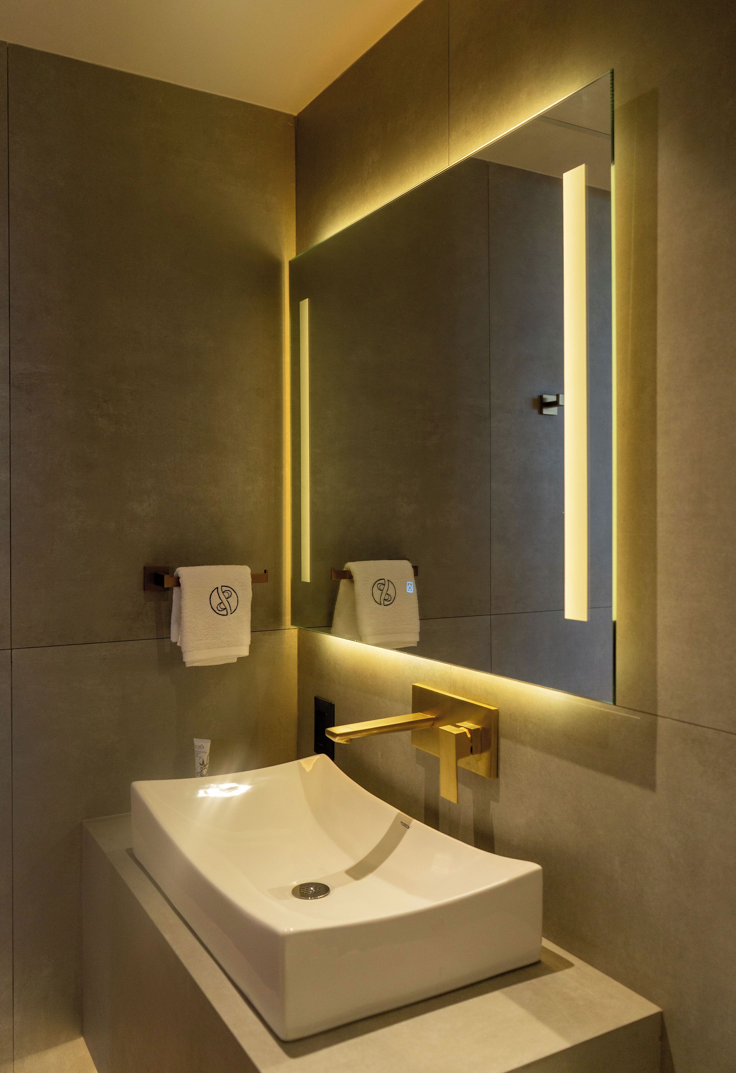 A modern bathroom with a large mirror, a white sink, and a towel rack.