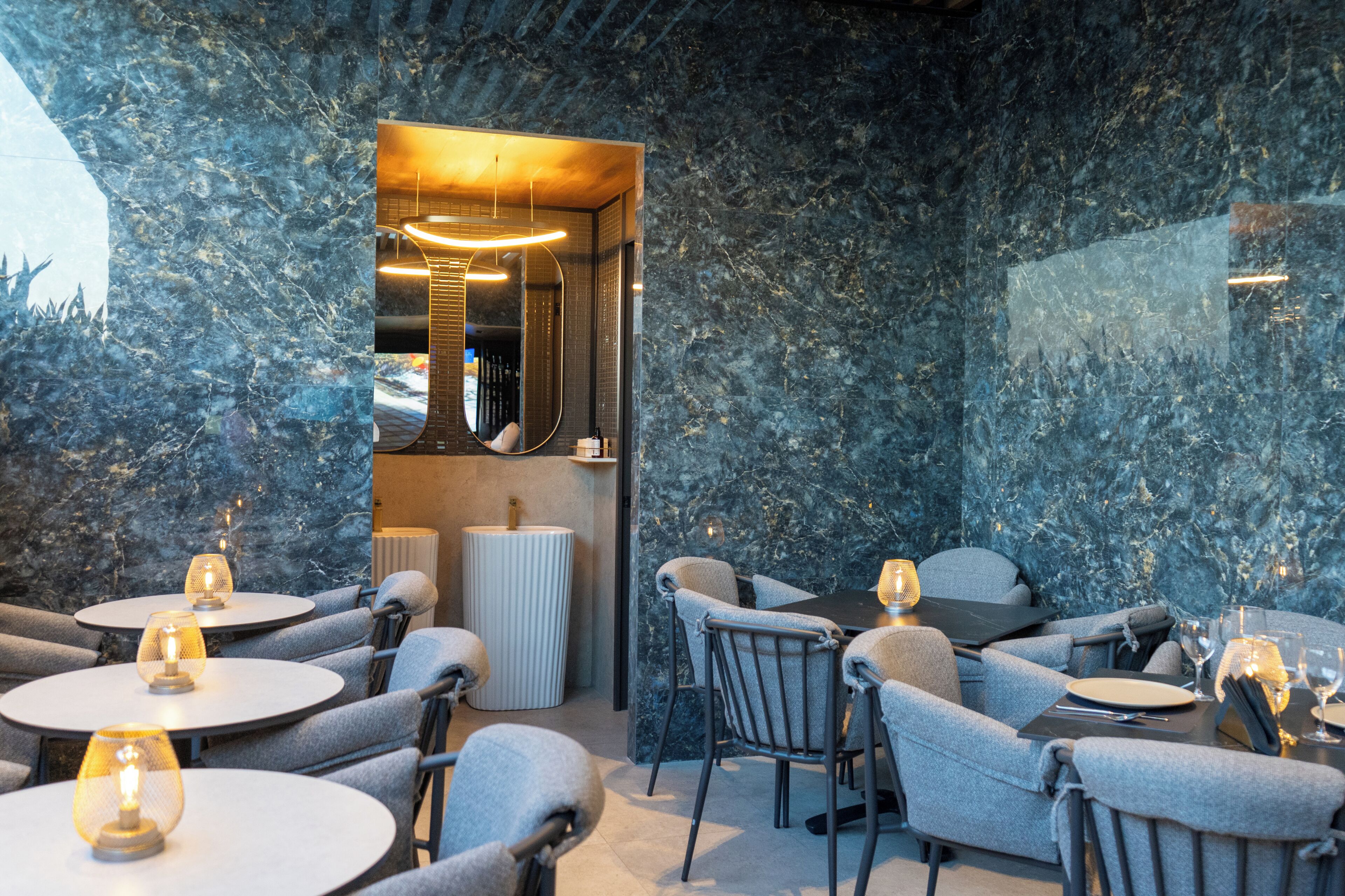 Un espace repas moderne avec des murs en marbre, des tables rondes et des sièges confortables.
