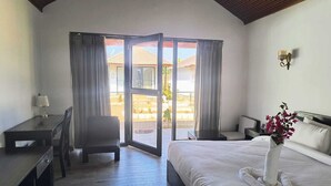 A hotel room with a bed, a desk, a chair, a nightstand, and a large sliding glass door leading to a balcony.