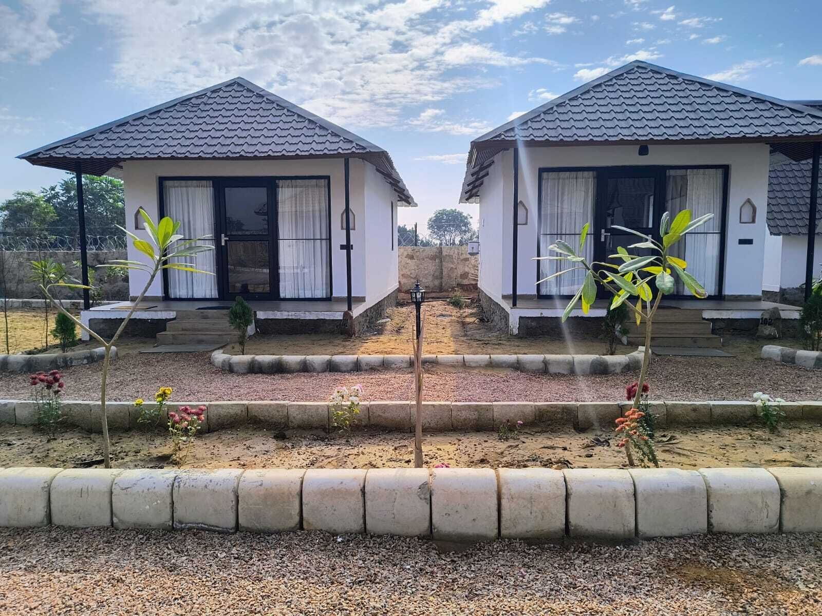 Deux petites maisons identiques, toutes deux blanches et dotées de toits en tuiles, chacune ayant un petit porche et une fenêtre.